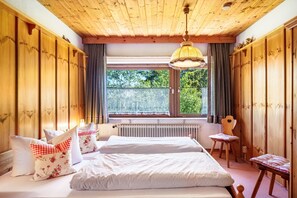 A wooden-paneled room with a bed, a chair, a window, and a radiator.