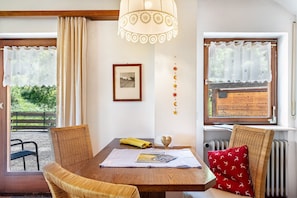 Een eetruimte met rieten stoelen, een houten tafel, een hanglamp en een raam met gordijnen.