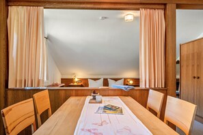 A dining area with a wooden table, chairs, a window with curtains, a small table with a candle, and a wall-mounted light fixture. - Apartment 'Dahlie, 90qm' with Mountain View, Shared Garden and Wi-Fi (Feldberg (Schwarzwald))