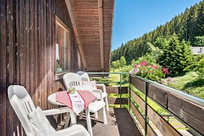 A wooden balcony with white plastic chairs and a table, overlooking a forested hillside. - Apartment 'Dahlie, 90qm' with Mountain View, Shared Garden and Wi-Fi (Feldberg (Schwarzwald))