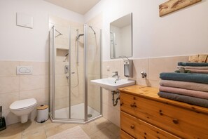 A bathroom with a glass-enclosed shower, a sink, a toilet, and a wooden vanity with towels. - Holiday Apartment 'Landnest' with Mountain View, Balcony and Wi-Fi (Prutting)