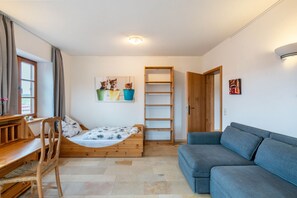 Una stanza con un letto, un divano blu, una scrivania in legno, una sedia, uno scaffale con piante e una porta.