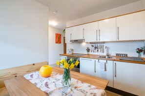 Una cucina moderna con mobili bianchi, un piano di lavoro in legno e un vaso con fiori gialli su un tavolo.
