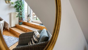 Une pièce avec un fauteuil en osier, une plante en pot, un radiateur et une fenêtre donnant sur un beau paysage.