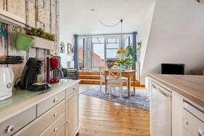Eine Küche mit Holzausstattung, ein Essbereich mit Tisch und Stühlen sowie ein Ausblick durch große Fenster.