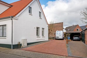 Un bâtiment blanc avec un toit recouvert de tuiles rouges, un mur en briques et une entrée de garage.