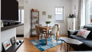 A modern living room with a TV, a dining table with chairs, a sofa, and a coffee table. - Holiday Apartment 'Tu Huus' with Private Garden and Wi-Fi (Wesselburen)