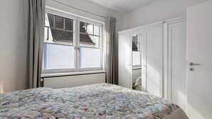 A bedroom with a bed, a window with blinds, a radiator, and a wardrobe. - Holiday Apartment 'Tu Huus' with Private Garden and Wi-Fi (Wesselburen)