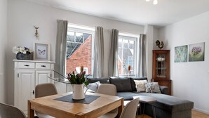 A modern living room with a dining table, grey sofa, and a small side table. - Holiday Apartment 'Tu Huus' with Private Garden and Wi-Fi (Wesselburen)
