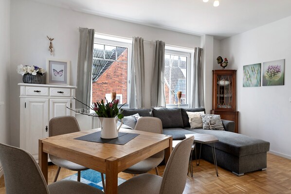 Un salon moderne avec une table à manger, un canapé gris et une petite table d’appoint.