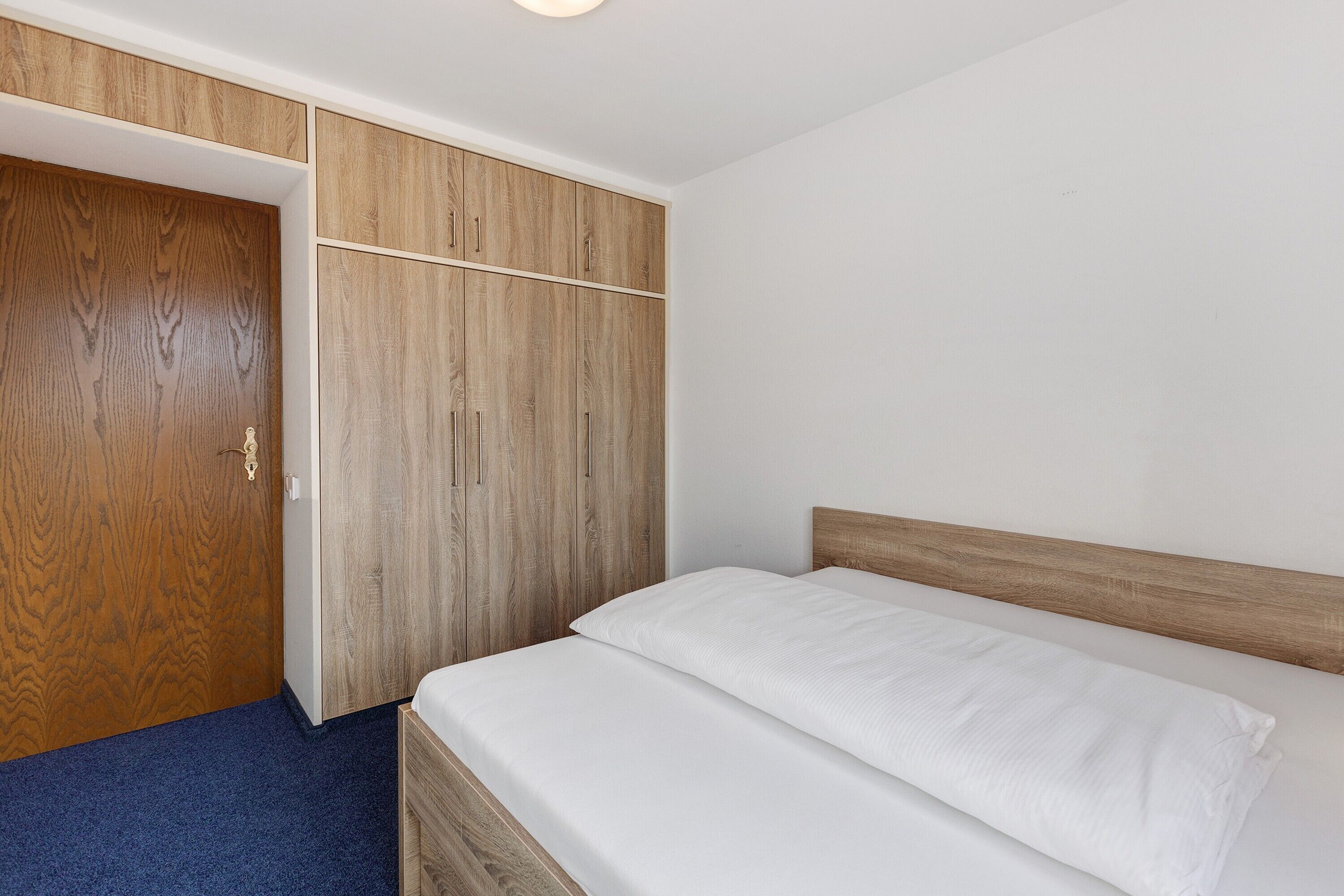 A bedroom with a bed, wooden wardrobe, and a blue carpet.