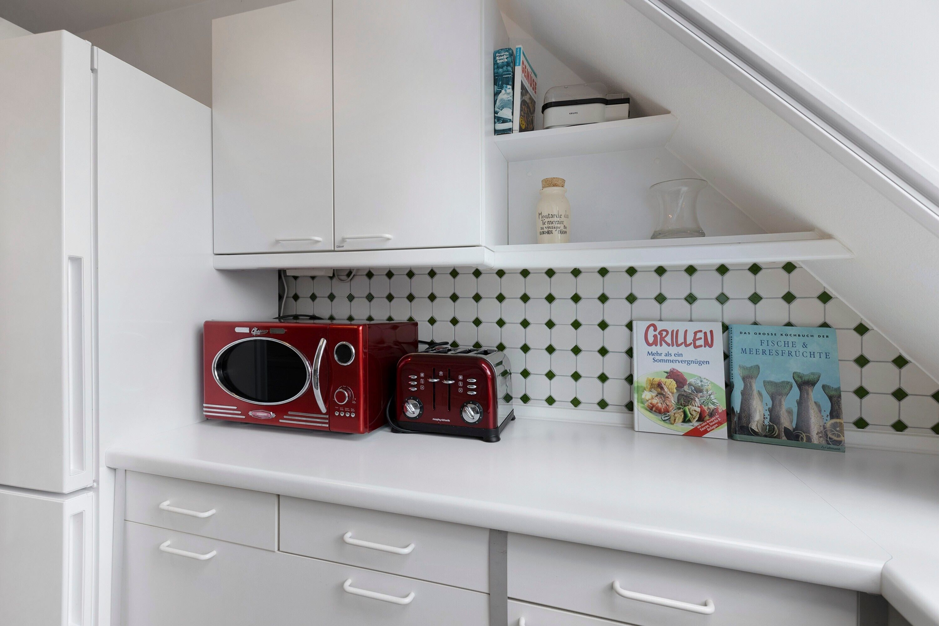 Une cuisine avec des meubles blancs, un four à micro-ondes, un grille-pain et deux livres de recettes posés sur le plan de travail.