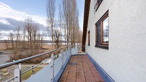 A balcony with a metal railing, a white building, and a view of trees and a distant landscape. - Apartment 'Untersee' with Lake View, Private Terrace and Wi-Fi (Moos)