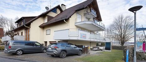 A two-story building with a balcony, a parked car, and a street sign.