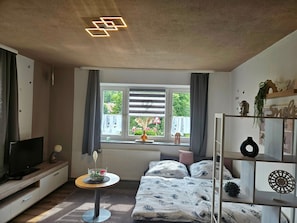 Une chambre à coucher avec un lit, une télévision, une petite table et une fenêtre avec des rideaux.