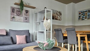 A modern living room with a grey sofa, a round wooden table with a white basket, grey chairs, and a white shelving unit.