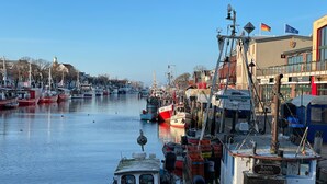 Un port amb embarcacions amarrades, un edifici amb un rètol que diu 'Barth Warenmünde' i un cel serè.