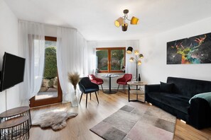 Uma sala de estar moderna com um sofá preto, uma TV, um espaço de jantar com mesa e cadeiras e uma janela grande com cortinas.