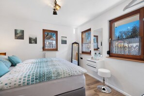 Un dormitorio con una cama, un aparador, un espejo y dos ventanas.
