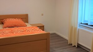 Una camera da letto con un letto, un comodino, una finestra con tende e un termosifone.