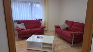 A living room with two red sofas, a white coffee table, and a window with sheer curtains. - Holiday Home 'Linde' with Private Garden (Westerburg)
