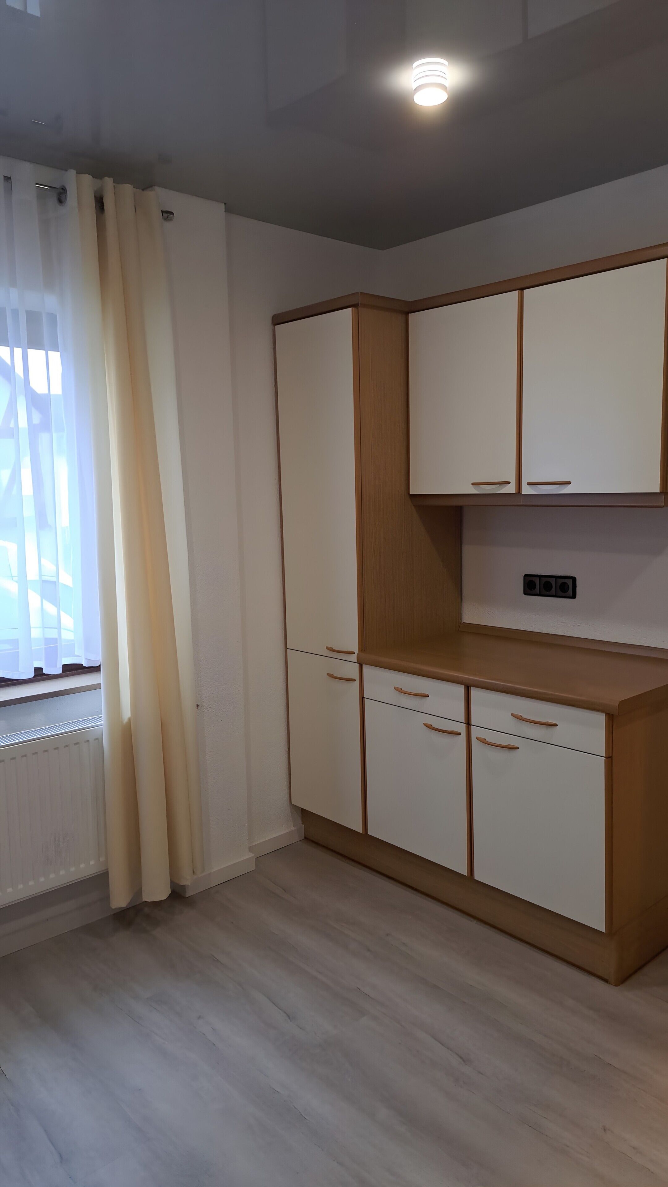 Une pièce avec une armoire blanche, un radiateur et une fenêtre ornée de rideaux légers.