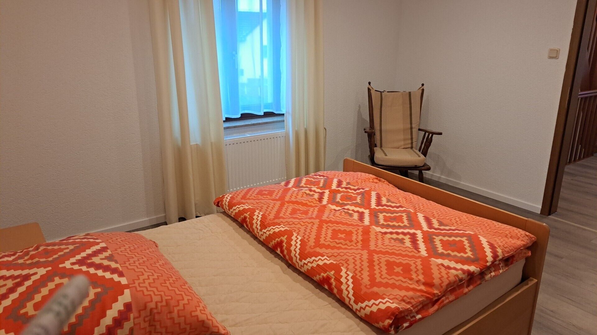 Ein Schlafzimmer mit zwei Betten, einem Sessel und einem Fenster mit Vorhängen.