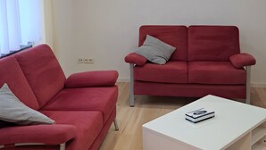 Un soggiorno moderno con un divano rosso, una poltrona coordinata, un tavolino da caffè bianco e illuminazione a soffitto incassata.