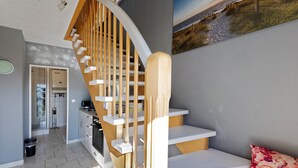 Un interior moderno con una escalera de madera curva, una zona de cocina y un espacio de estar con un sofá y un cojín decorativo.