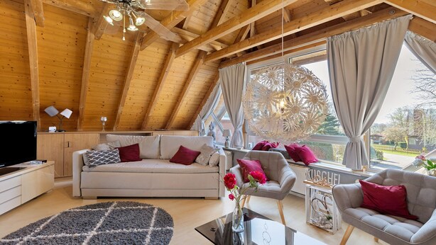 Una sala de estar moderna con techo de madera, un sofá, un sillón, una mesa de centro y un televisor.