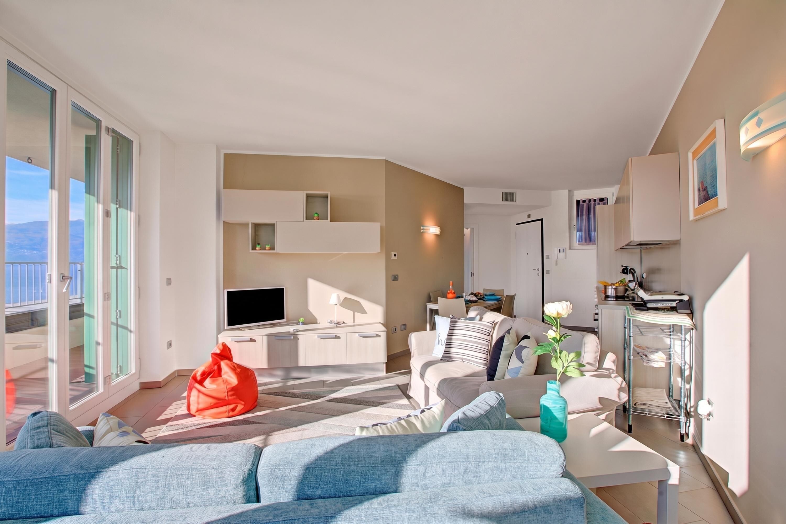 Un salon moderne avec un canapé, une table basse et un téléviseur. Il y a un balcon avec vue sur les montagnes.
