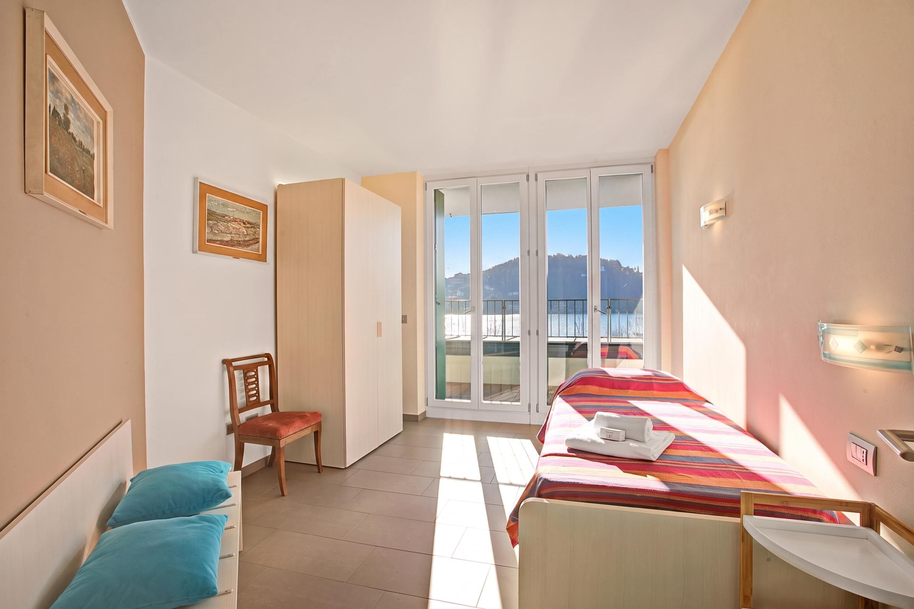 Una camera d'albergo con un letto, una sedia, un tavolo, una finestra vista e una porta che conduce a un'altra stanza.