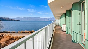 Ein Balkon mit Blick auf einen See und Berge, eine Holzterrasse und grüne Türen.