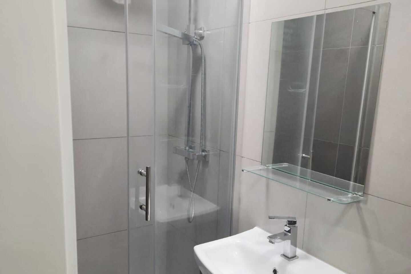 Ein modernes Badezimmer mit einer gläsernen Dusche, einer Glasablage und einem weißen Waschbecken.