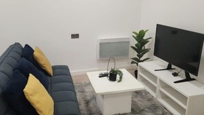 A living room with a dark blue sofa, a white coffee table, a flat-screen TV, and a small plant. - 1 Bed Studio - Central, Free Parking (London)