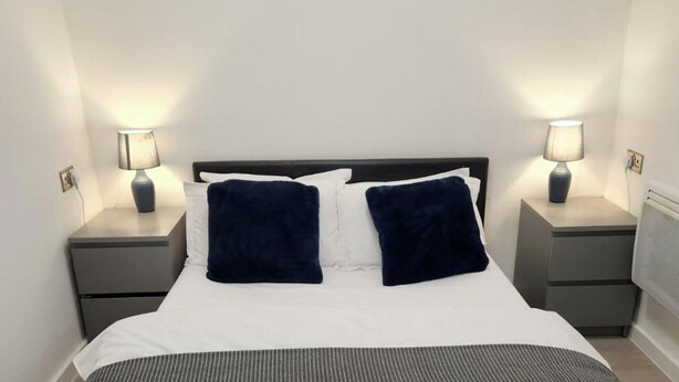A neatly made bed with two pillows, two bedside lamps, and a painting on the wall. - 1 Bed Studio - Central, Free Parking (London)