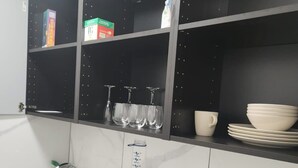 A kitchen with a microwave, toaster, and shelves with dishes and glasses. - 1 Bed Studio - Central, Free Parking (London)