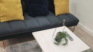 A dark grey sofa with two yellow cushions and a white coffee table with a small potted plant and a remote control. - 1 Bed Studio - Central, Free Parking (London)