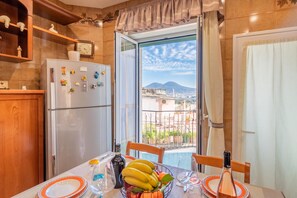 Une cuisine équipée d’un réfrigérateur, d’une table à manger avec des chaises, et offrant une vue sur le paysage urbain à travers une porte vitrée.