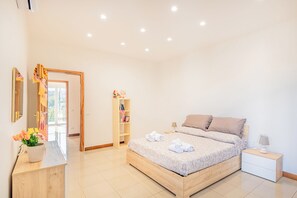 Une chambre à coucher avec un lit en bois, des tables de chevet, une commode, un miroir, une étagère avec des livres et une plante en pot.