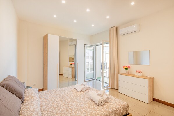 A modern bedroom with a bed, a dresser, a mirror, and a sliding glass door leading to a balcony.