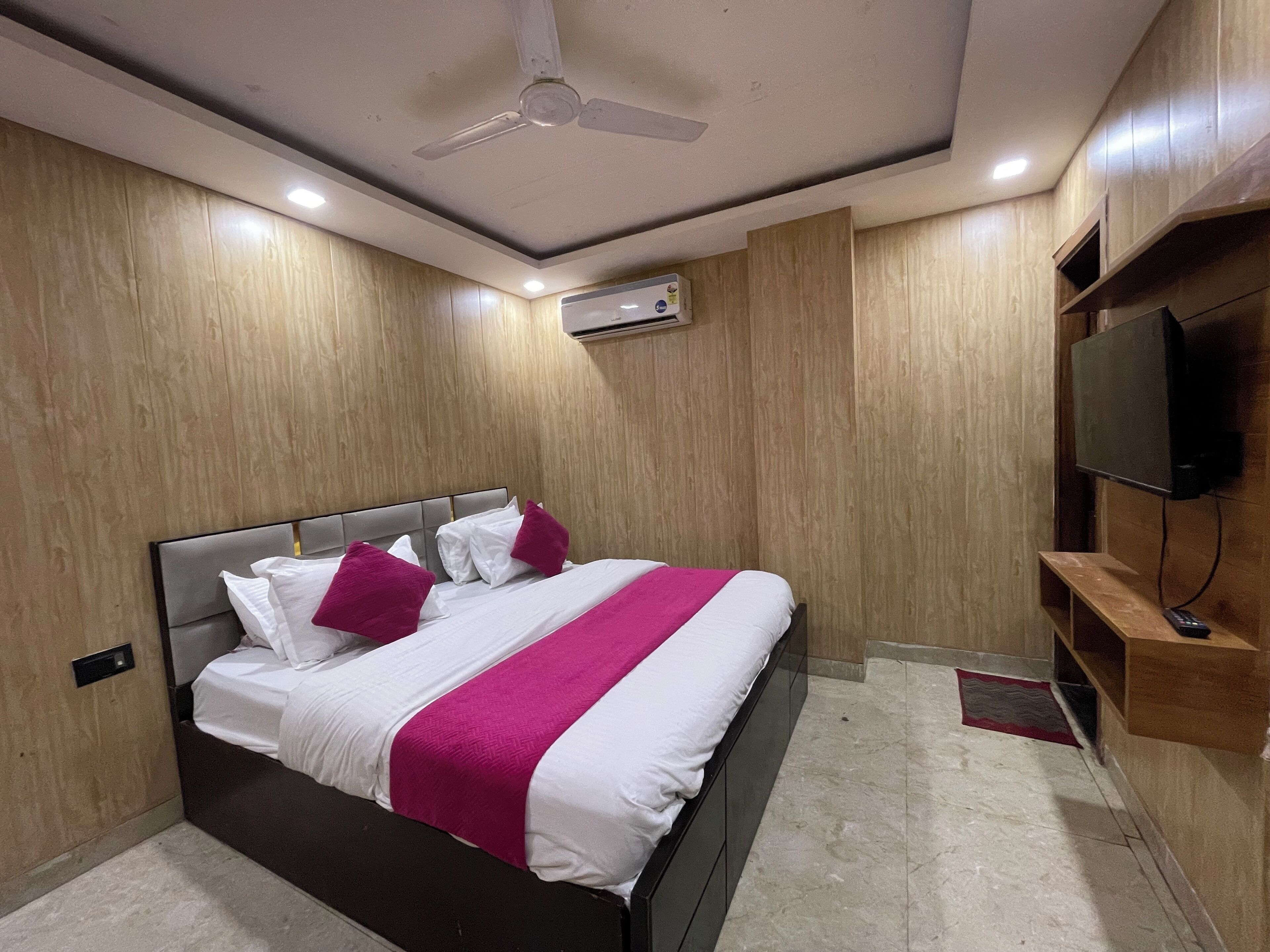 Una habitación de hotel moderna con una cama grande, paneles de madera, un ventilador de techo, unidad de aire acondicionado y un televisor montado.