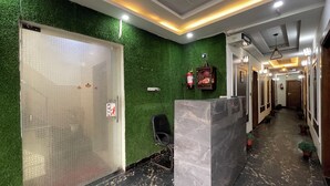 Zona de recepción con pared verde, mostrador de mármol y un pasillo con puertas.