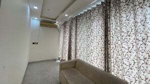 Una habitación con sofá, cortinas estampadas, suelo de baldosas e iluminación empotrada en el techo.