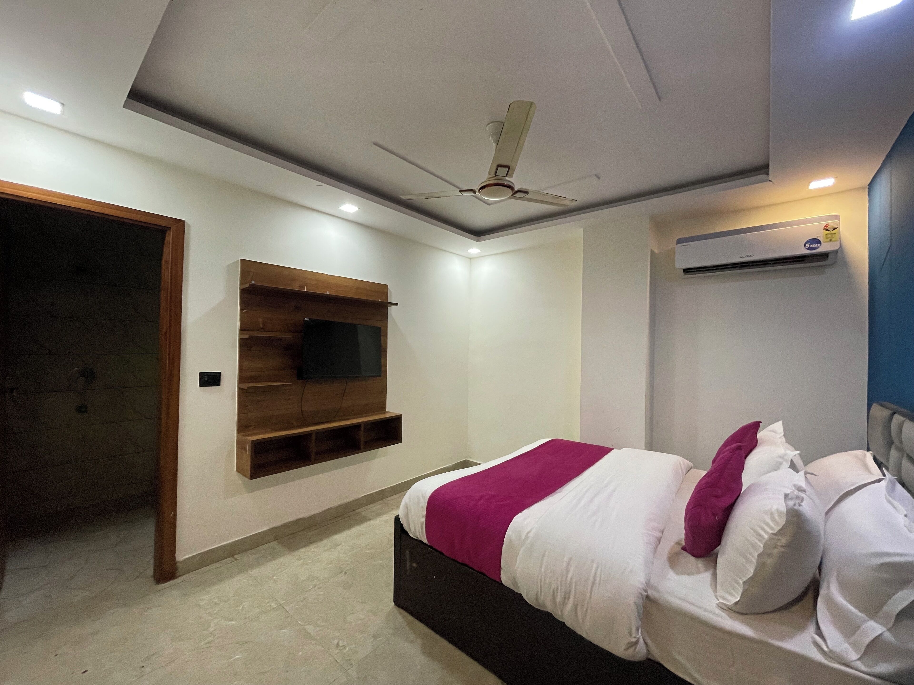 A bedroom with a bed, a mounted TV, an air conditioning unit, and a ceiling fan.