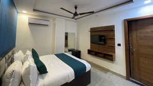 Un dormitorio moderno con cama, ventilador de techo, equipo de aire acondicionado, televisor montado en un panel de madera y puerta de madera.