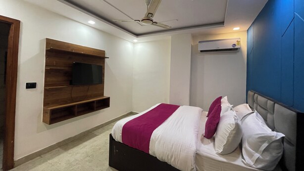 A bedroom with a bed, a mounted TV, a ceiling fan, and an air conditioning unit. - Hotel Heaven  Pacific Mall Subhash Nagar (New Delhi)