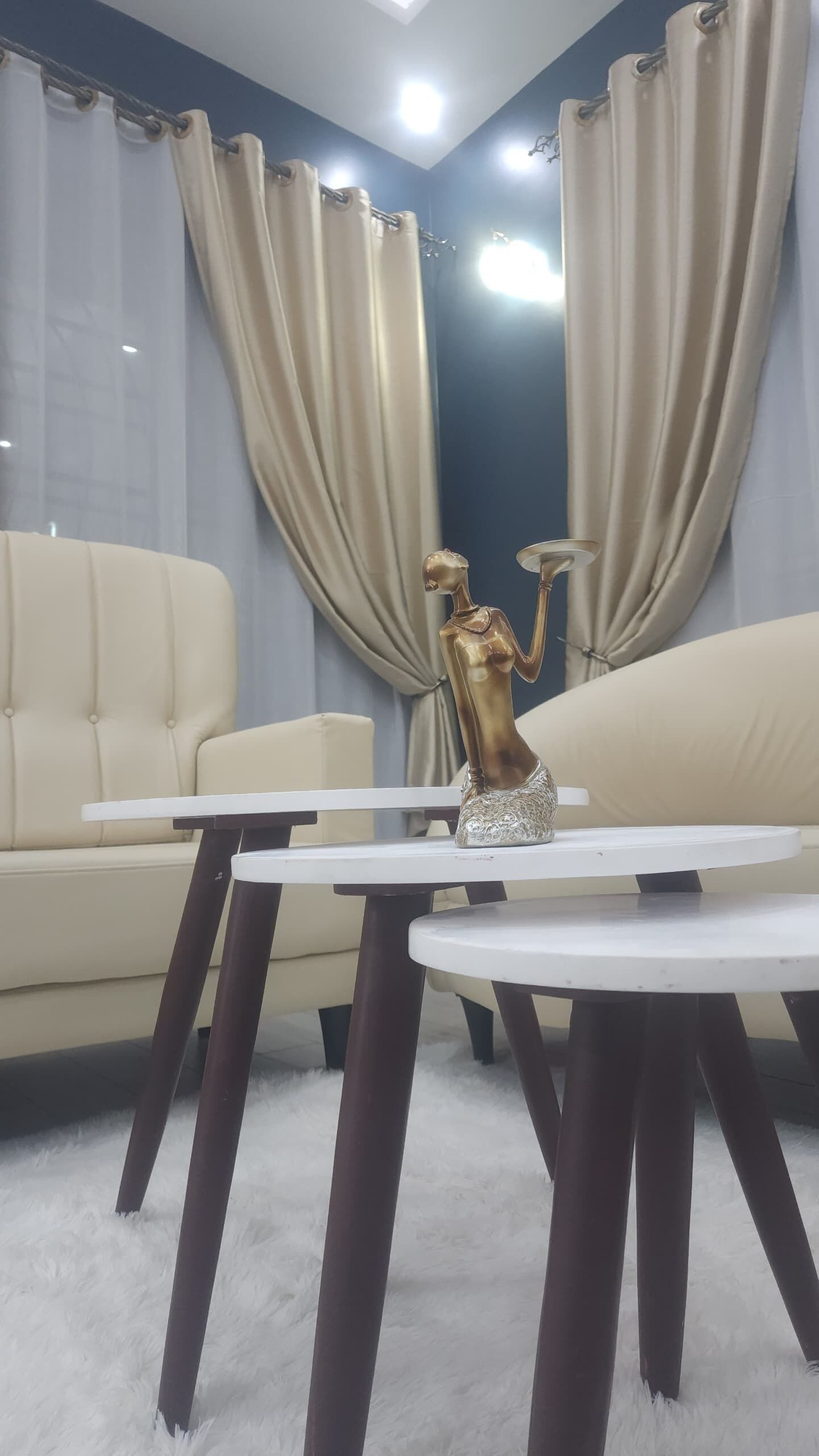 Ein modernes Wohnzimmer mit einem beigen Sofa, einem kleinen weißen Tisch und einer dekorativen goldfarbenen Statue.