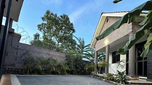 A paved courtyard with a stone floor, surrounded by greenery and a building with a light fixture. - Luxury home,  located in a quiet and calm area, Home away from home. (Entebbe)