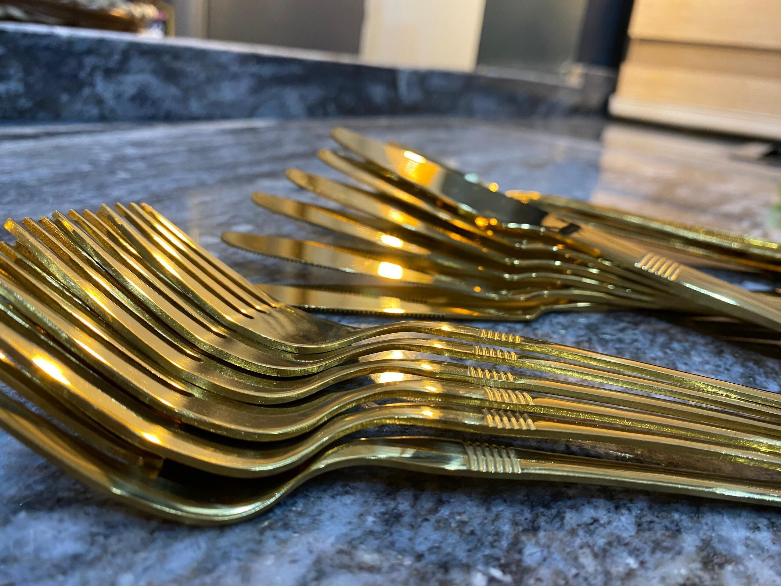 A stack of gold-colored forks and knives on a kitchen counter.